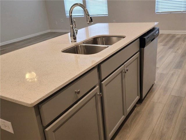 kitchen with gray cabinetry, a kitchen island with sink, a sink, and dishwasher
