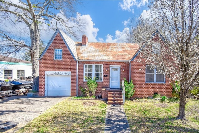 tudor house with gravel driveway, a garage, brick siding, and a chimney