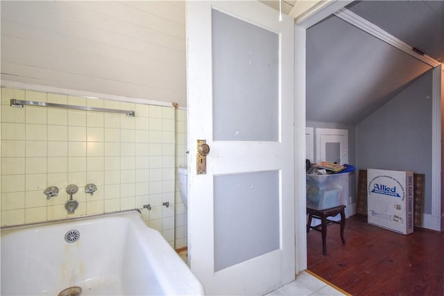 bathroom with lofted ceiling, wood finished floors, and a tub to relax in