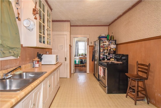 kitchen featuring a wainscoted wall, a sink, wallpapered walls, gas range, and white microwave