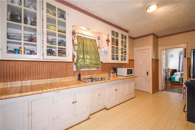 kitchen with white microwave, light floors, a sink, white cabinets, and a textured ceiling