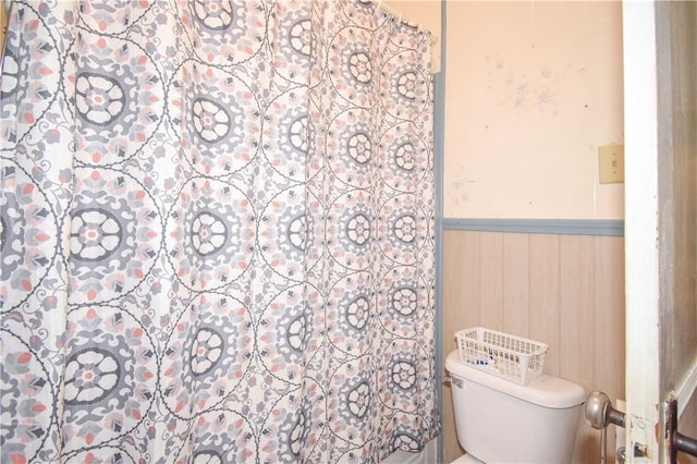 bathroom featuring a wainscoted wall, toilet, wooden walls, and a shower with curtain