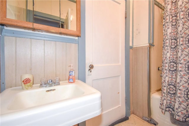 full bathroom with shower / bath combo with shower curtain, wood walls, and a sink