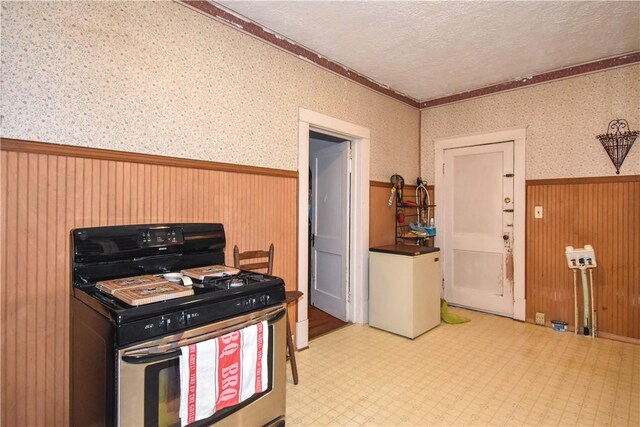 kitchen with stainless steel gas range, wallpapered walls, wainscoting, a textured ceiling, and tile patterned floors