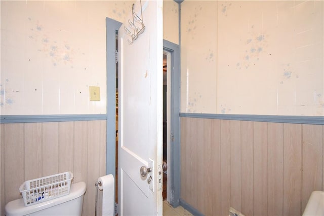 bathroom with wooden walls, wainscoting, and toilet