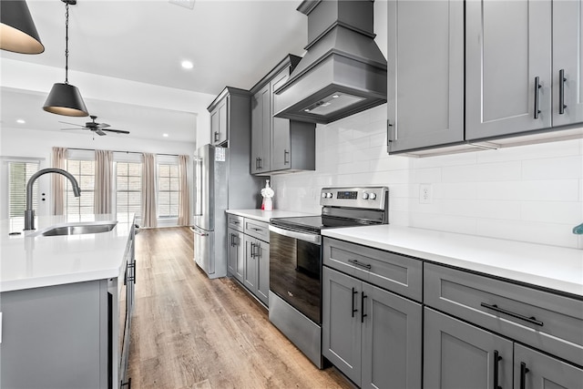 kitchen featuring premium range hood, sink, gray cabinetry, light wood-type flooring, and appliances with stainless steel finishes