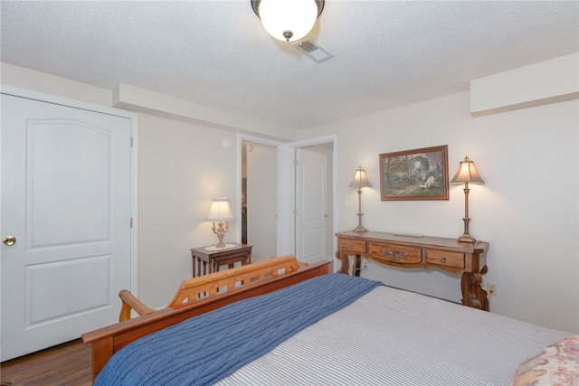 bedroom with a textured ceiling, wood finished floors, and visible vents