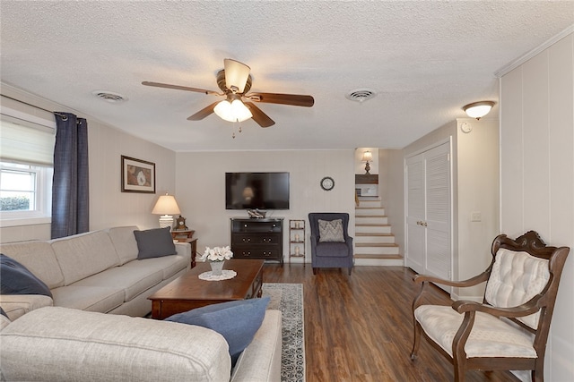 living room featuring stairs, visible vents, a textured ceiling, and wood finished floors