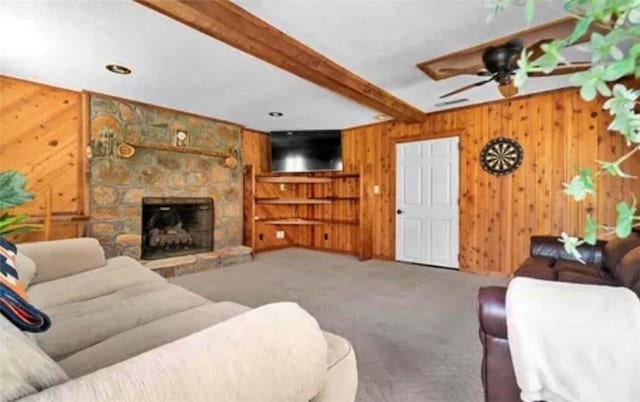 carpeted living room with beamed ceiling, a fireplace, wooden walls, and ceiling fan