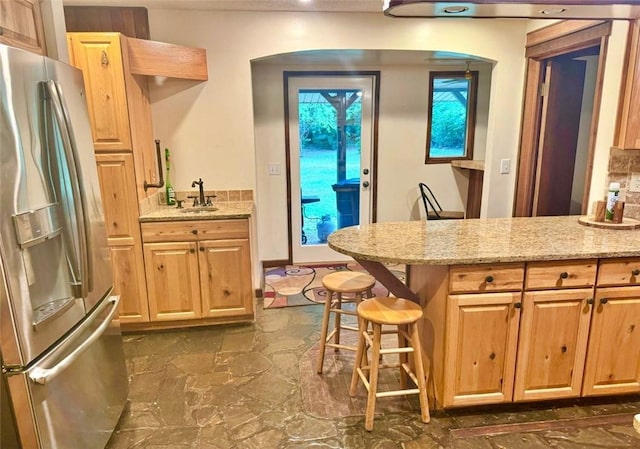 kitchen with stainless steel fridge, light stone counters, sink, and a breakfast bar area