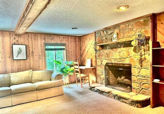 living room with carpet, a textured ceiling, beamed ceiling, a stone fireplace, and wood walls