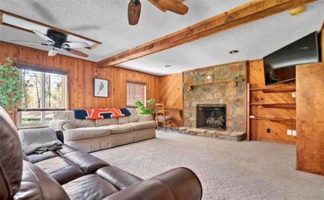 carpeted living room with wood walls, beam ceiling, and a stone fireplace