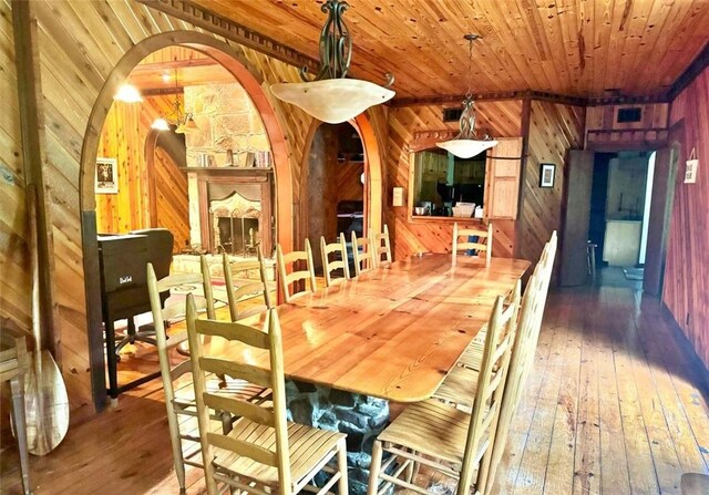 dining room featuring wood-type flooring, wooden walls, a stone fireplace, and wooden ceiling