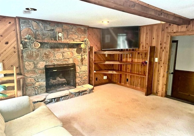 living room with beamed ceiling, wood walls, a stone fireplace, and light carpet