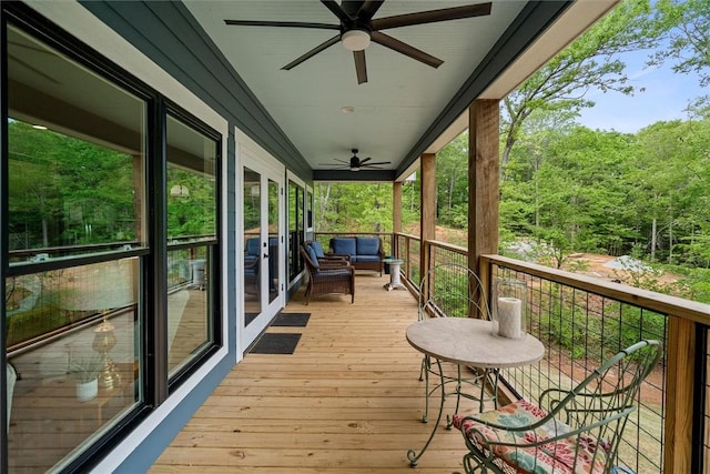wooden deck with a view of trees, ceiling fan, and an outdoor hangout area