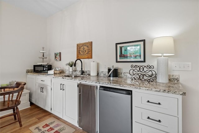 kitchen featuring fridge, light stone counters, a sink, light wood finished floors, and white cabinetry