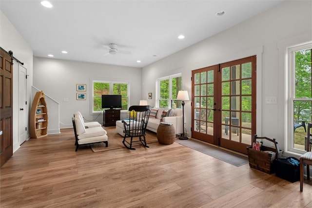 living area featuring light wood-style floors, recessed lighting, a barn door, french doors, and a ceiling fan