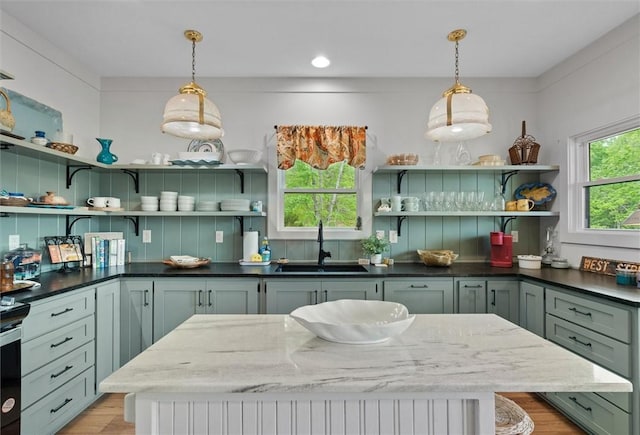 kitchen with a sink, hanging light fixtures, open shelves, and light wood-type flooring