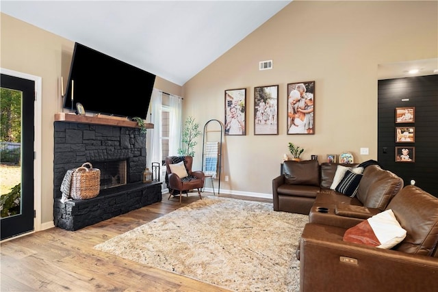 living room featuring a stone fireplace, plenty of natural light, high vaulted ceiling, and hardwood / wood-style flooring