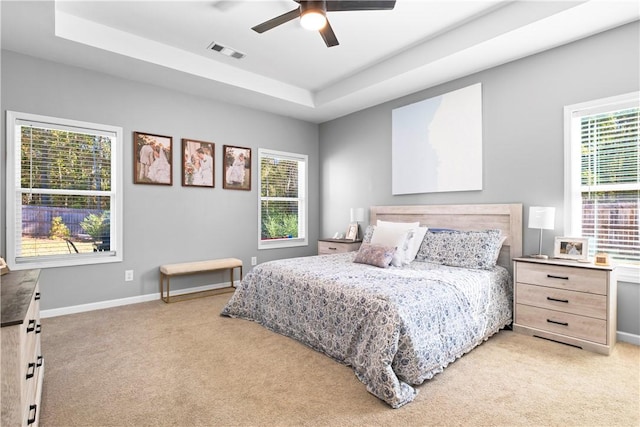 bedroom with ceiling fan, multiple windows, and a tray ceiling