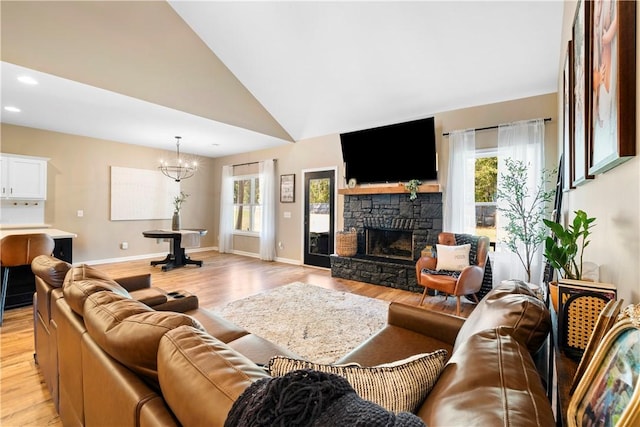 living room featuring light wood-type flooring, an inviting chandelier, a stone fireplace, and high vaulted ceiling