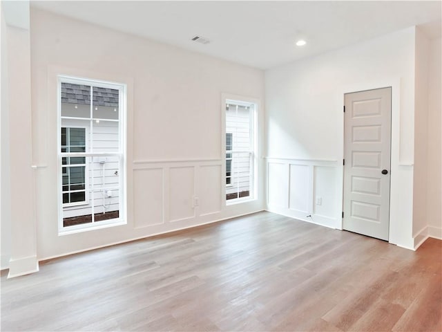 empty room with visible vents, wainscoting, recessed lighting, light wood-style floors, and a decorative wall