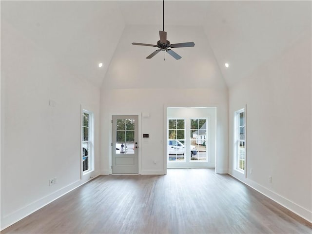 unfurnished living room with ceiling fan, high vaulted ceiling, baseboards, and wood finished floors