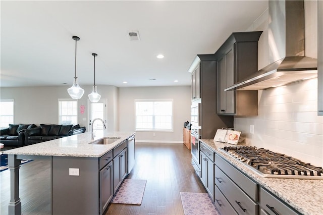 kitchen featuring a center island with sink, sink, wall chimney exhaust hood, gray cabinets, and stainless steel appliances