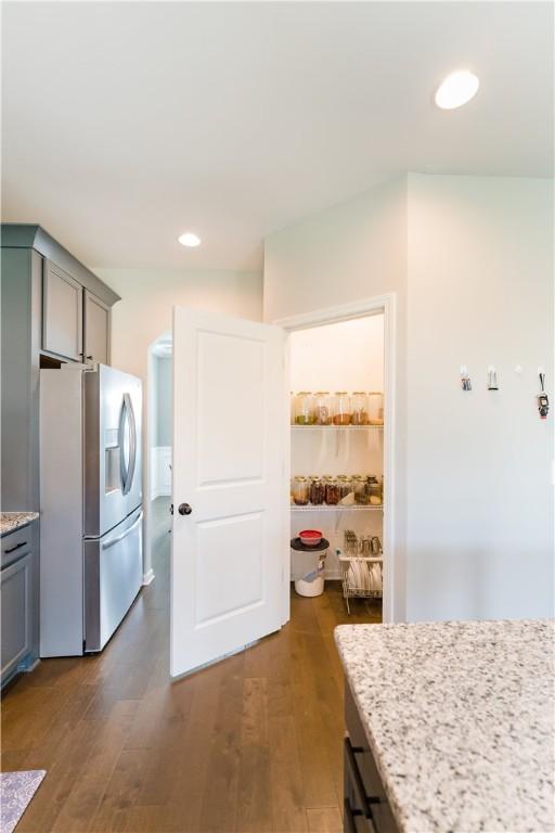 kitchen with light stone countertops, gray cabinets, stainless steel fridge with ice dispenser, and dark wood-type flooring