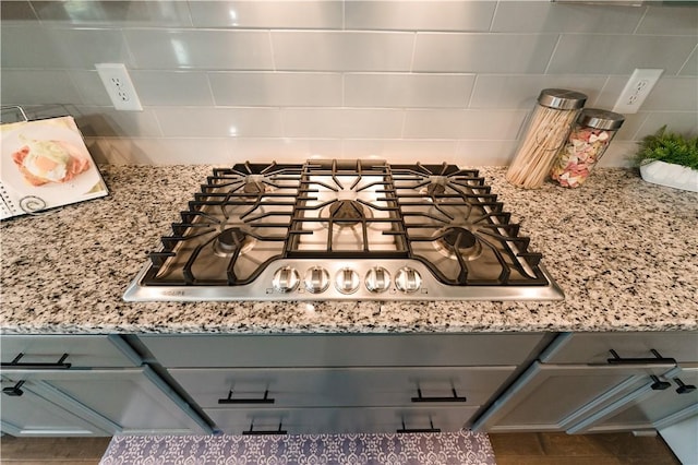 room details with decorative backsplash, light stone countertops, gray cabinets, and stainless steel gas cooktop