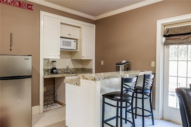 56 Peachwood Dr, Tallassee, AL 36078 - kitchen featuring freestanding refrigerator, white microwave, crown molding, white cabinets, and a kitchen breakfast bar