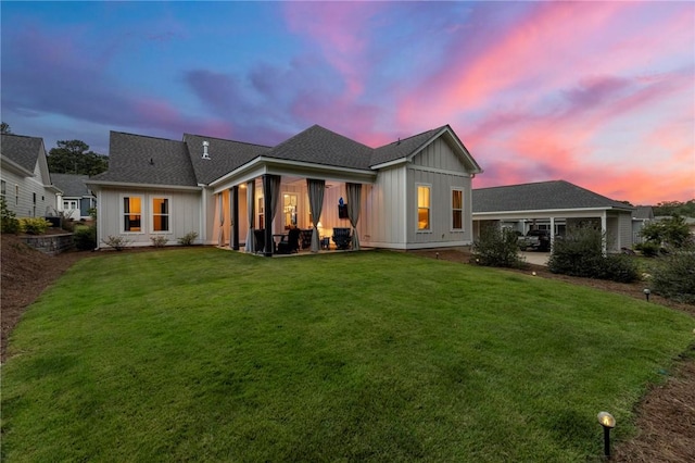 back house at dusk featuring a lawn