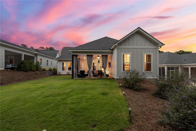 back house at dusk featuring a lawn