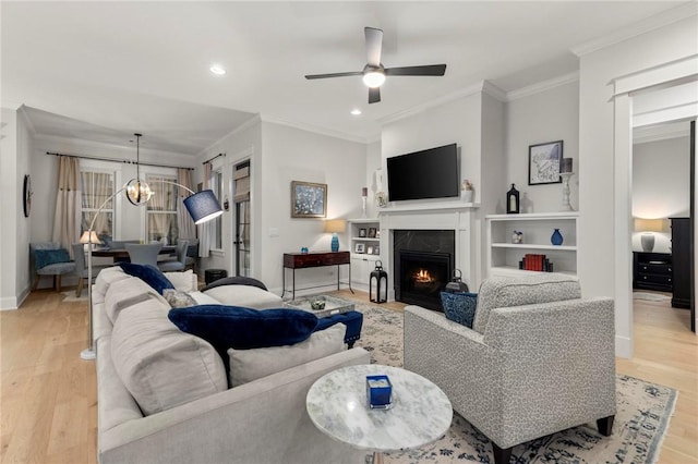 living room with a fireplace, light wood-type flooring, ceiling fan with notable chandelier, and crown molding