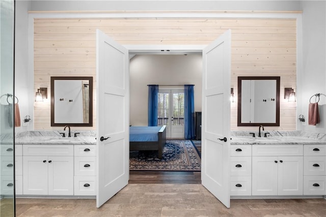 full bath featuring two vanities, a sink, and wood walls