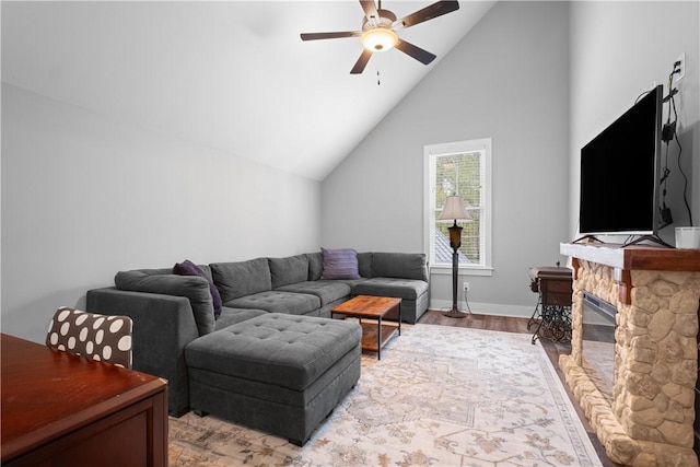 living area featuring light wood finished floors, baseboards, a fireplace, a ceiling fan, and vaulted ceiling