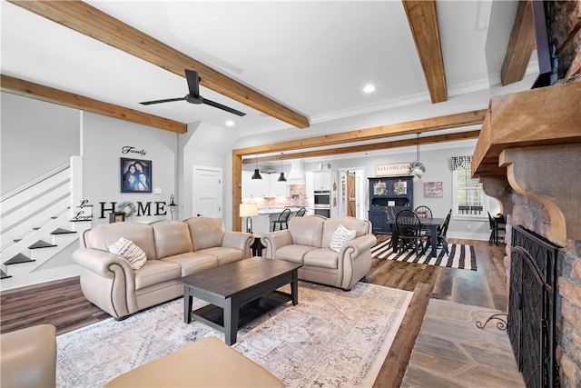 living area with stairs, ceiling fan, wood finished floors, and beamed ceiling