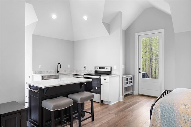 kitchen featuring white cabinets, wood finished floors, stainless steel appliances, a breakfast bar area, and vaulted ceiling