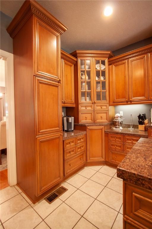 1849 Stoneridge Dr, Auburn, AL 36830 - kitchen with light tile patterned floors, brown cabinets, glass insert cabinets, and dark stone counters