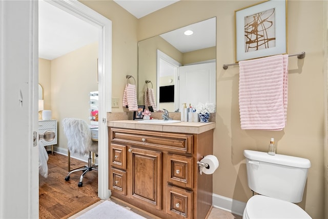 half bath with baseboards, vanity, toilet, and wood finished floors