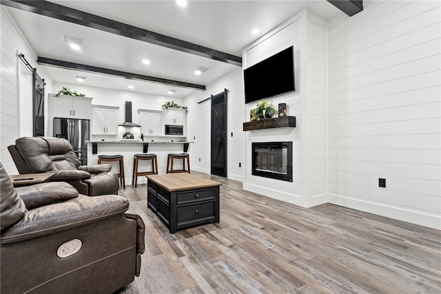 living room with beamed ceiling, a barn door, and light hardwood / wood-style floors