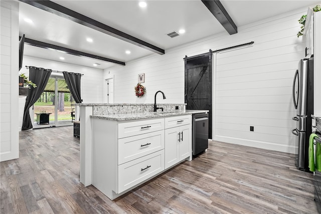 kitchen featuring light stone countertops, stainless steel appliances, a barn door, beamed ceiling, and white cabinets