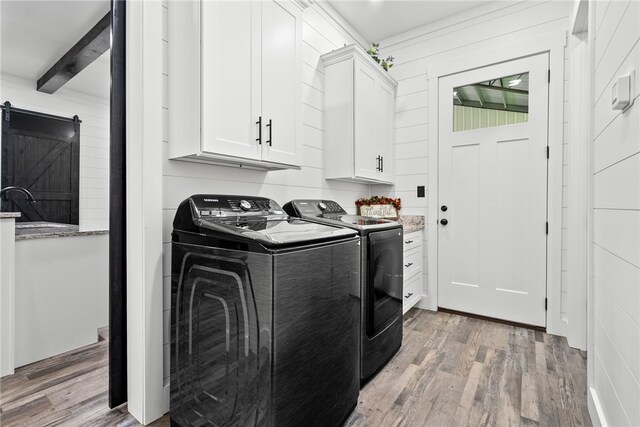 laundry area featuring a barn door, cabinets, light hardwood / wood-style floors, and washing machine and clothes dryer