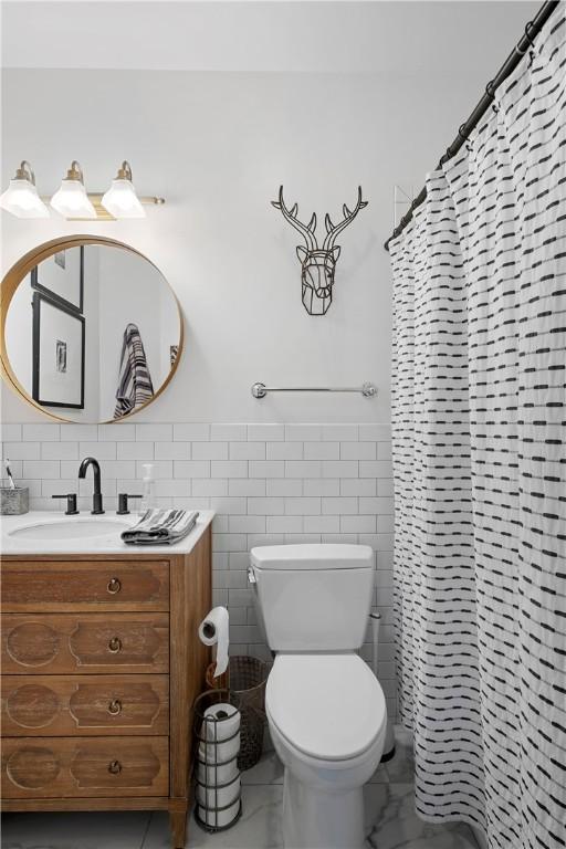 bathroom featuring walk in shower, vanity, toilet, and tile walls