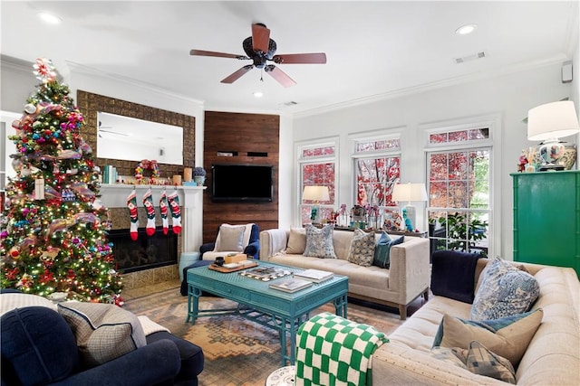 living room with ceiling fan, crown molding, and a tiled fireplace