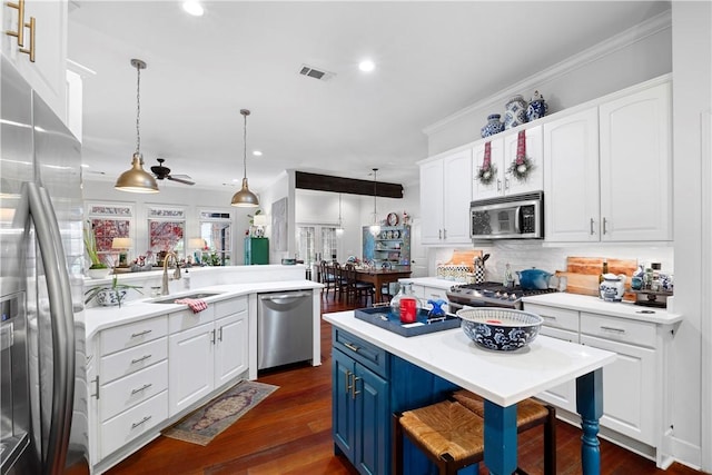 kitchen featuring appliances with stainless steel finishes, blue cabinets, sink, decorative light fixtures, and white cabinets