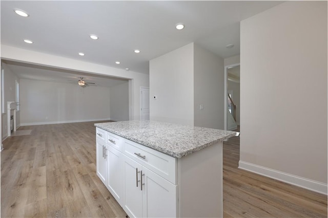 kitchen featuring ceiling fan, light wood-style flooring, white cabinets, a center island, and baseboards