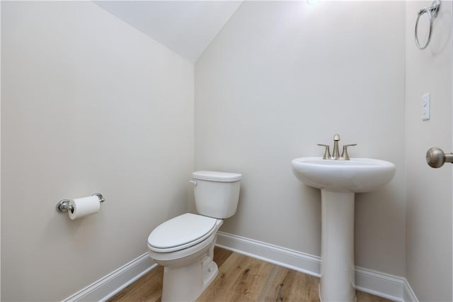 half bath with baseboards, vaulted ceiling, toilet, a sink, and wood finished floors