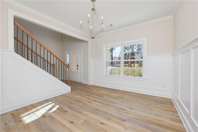 interior space with light wood-style floors, a decorative wall, an inviting chandelier, crown molding, and stairs