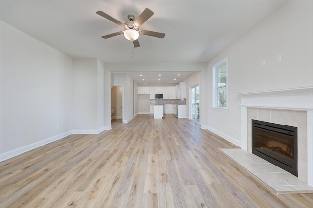 unfurnished living room with a tile fireplace, baseboards, recessed lighting, ceiling fan, and light wood finished floors